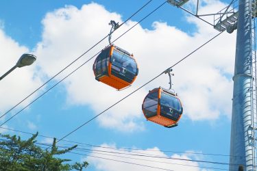 Kötélpályás kabinok közlekednek nagyvárosi környezet felett, a városi közlekedési hálózat részeként.