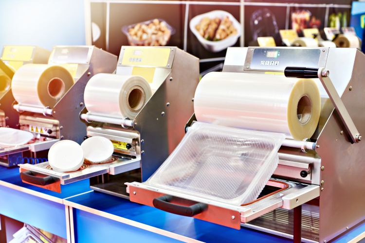 Ipari tálcazáró gépsor fóliatekercsekkel egy szakmai kiállításon.