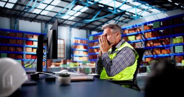 Raktári környezetben dolgozó szakember számítógép előtt, háttérben tárolt áruk.