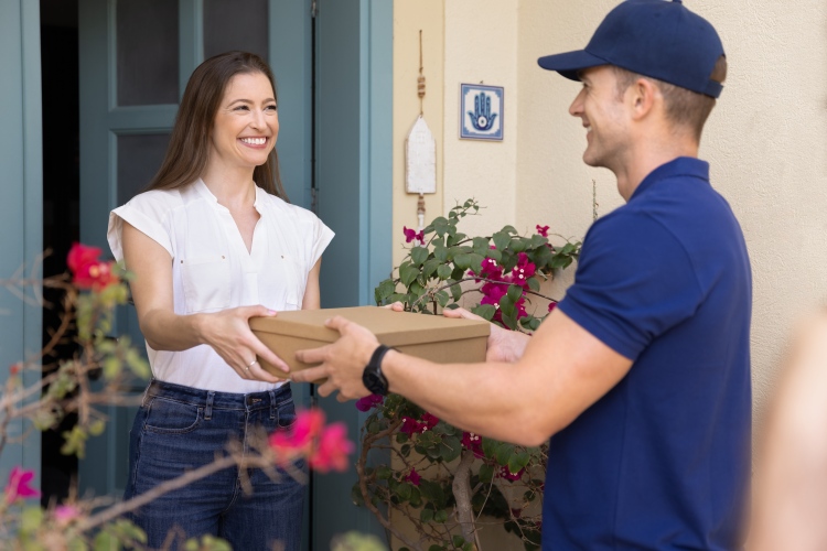 Futár ad át egy kartondobozt egy vásárlónak házhoz szállítás közben, az e-kereskedelmi csomagolás tipikus helyzetében.