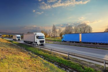 Több nyerges vontató halad autópályán, jól érzékeltetve a közúti áruszállítás költség- és szabályozási környezetét.