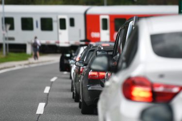 Autók várakoznak a vasúti átjárónál, miközben a háttérben vonat halad át.