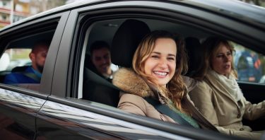 Mosolygó utasok ülnek egy személyautóban, amely a megosztott vállalati mobilitás illusztrációjaként használható.