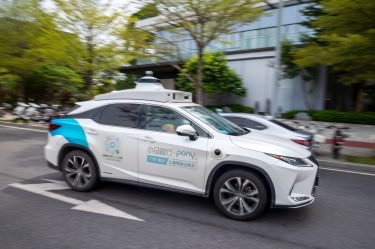 Önvezető rendszerrel felszerelt Toyota bZ4X halad városi környezetben, tetőre szerelt szenzorokkal.