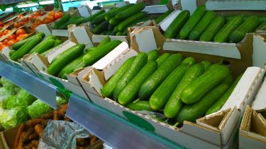 Friss uborkák láthatók kartondobozokban egy zöldséges pultban.