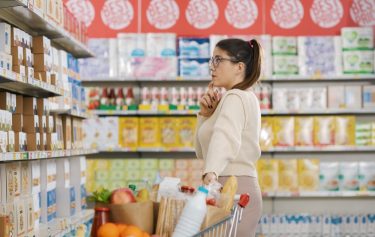 Egy vásárló termékeket néz egy élelmiszerbolt polcai előtt bevásárlókocsival.