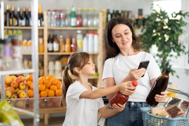 Egy nő és egy gyermek boltban terméket tartanak, miközben mobiltelefonnal információt keresnek a csomagoláson.