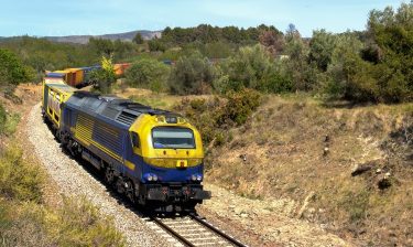 Tehervonat halad vidéki környezetben, dízelmozdonnyal vontatott áruszállító szerelvénnyel.