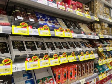 Csokoládék sorakoznak egy üzlet polcán, akciós címkékkel és védelmi megoldásokkal ellátva.