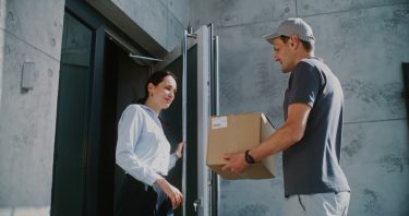 Futár ad át egy csomagot egy vásárlónak egy lakóépület bejáratánál.