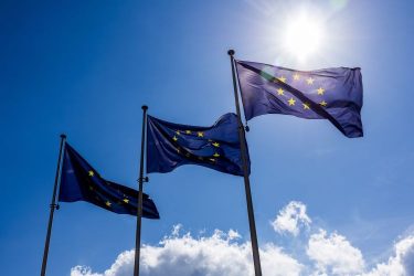 Európai zászlók az Európai Bizottság előtt a felhős kék ég alatt.